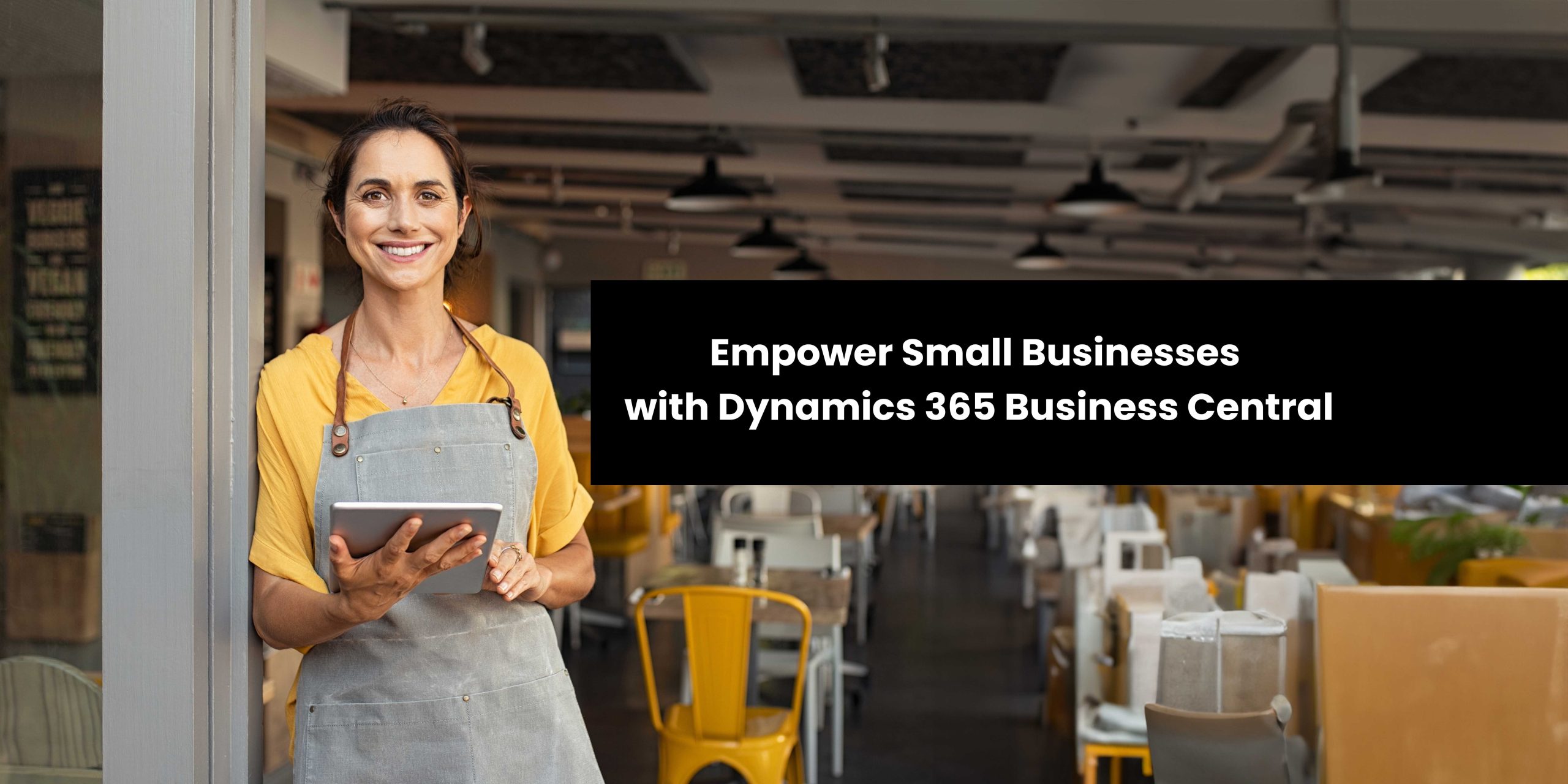 A smiling small business owner stands in a restaurant, holding a tablet and wearing an apron.