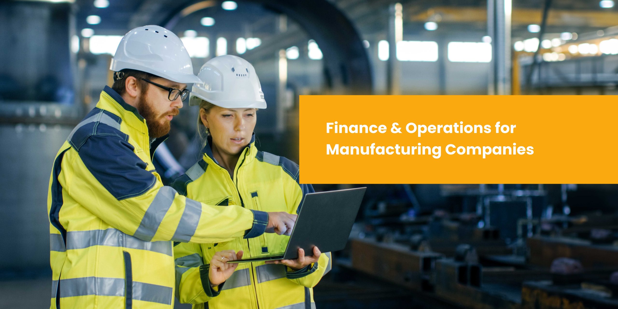 Two professionals in hard hats and high-visibility jackets collaborate over a laptop in a manufacturing environment.